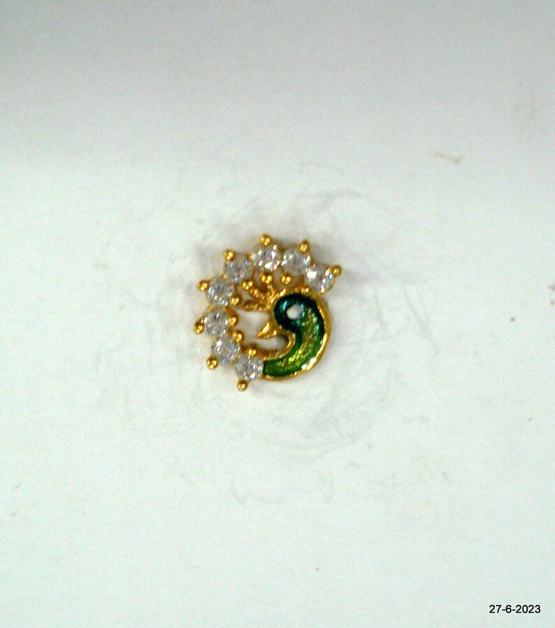 May include: A gold nose ring featuring a peacock design. The peacock is green and blue with white rhinestones around it.