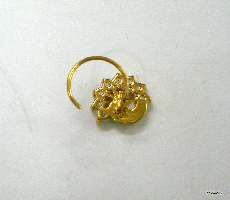 May include: A gold nose ring featuring a peacock design. The peacock is crafted from clear stones and has a gold body.