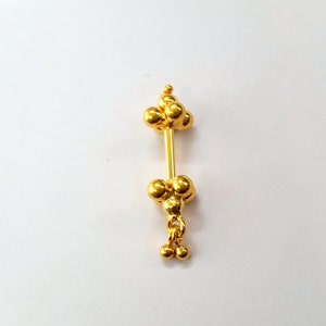 Op de afbeelding: Een gouden neusring met een cluster van kleine ronde kralen aan beide uiteinden en een hangende ketting met twee kralen aan de onderkant.