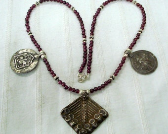 May include: A silver necklace with three pendants and purple beads. The pendants are ornate and feature detailed designs.