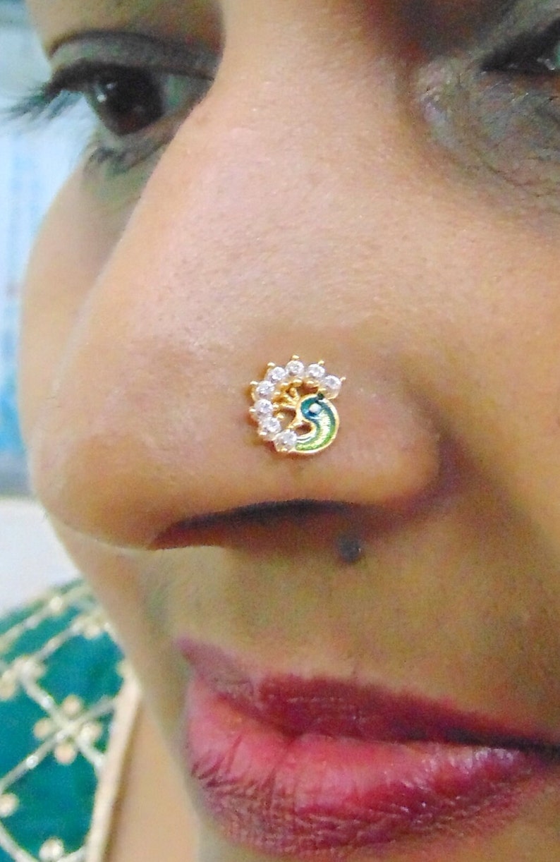 May include: A gold nose ring with a peacock design and white rhinestones.