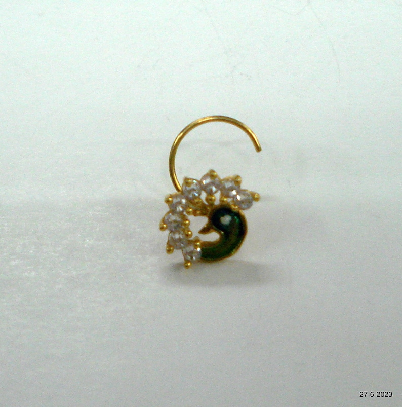 May include: A gold nose ring featuring a peacock design. The peacock is green and blue with white rhinestones.