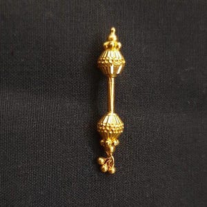 Op de afbeelding: Een gouden hanger met twee ronde, getextureerde ballen die met een dunne staaf zijn verbonden. De onderste bal heeft een kleine, hangende ketting met drie ronde kralen.