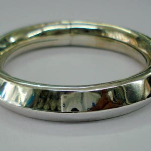 May include: A silver bangle bracelet with a smooth, rounded surface and a slightly textured design.