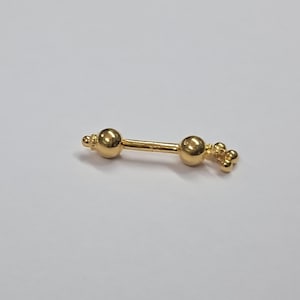 Op de afbeelding: Een goudkleurige barbell-stijl body piercing sieraden. De sieraden hebben twee bolvormige uiteinden en decoratieve clusters van kleine bollen. De barbell is gecentreerd op een witte achtergrond.