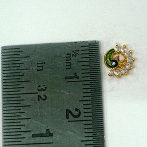 May include: A gold-toned nose ring featuring a peacock design. The peacock is green and blue with white rhinestones.