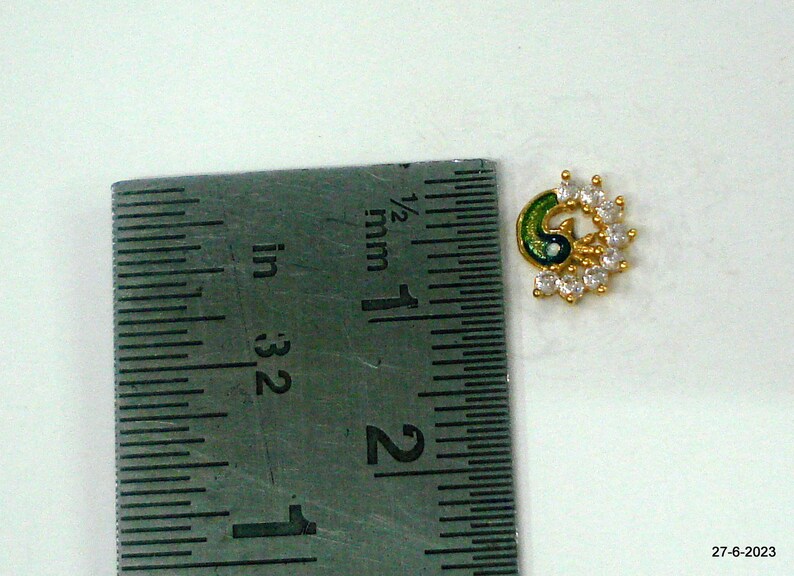 May include: A gold-toned nose ring featuring a peacock design. The peacock is green and blue with white rhinestones.