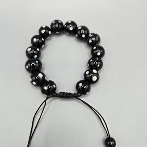 May include: A black bracelet with white polka dots and a black string closure.