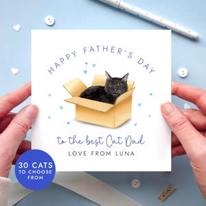 May include: A Father's Day card featuring a black cat in a cardboard box. The card reads "Happy Father's Day to the best Cat Dad, Love from Luna." The card is held by hands against a light blue background with heart-shaped decorations.