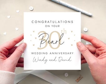 May include: A square white greeting card featuring the text CONGRATULATIONS ON YOUR 30th Pearl WEDDING ANNIVERSARY Wendy and David. The design includes a large beige number 30, black script lettering, and small beige heart icons surrounding the central text.