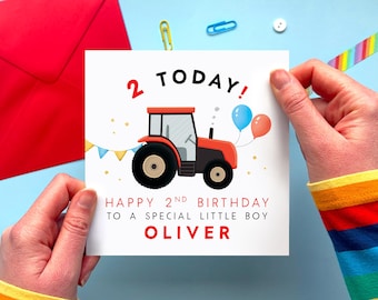 May include: A birthday card held by hands, featuring a red tractor with black wheels, blue and orange balloons, and the text "2 TODAY!" and "HAPPY 2ND BIRTHDAY TO A SPECIAL LITTLE BOY OLIVER" on a white background. A red envelope is visible.