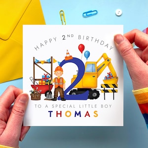 May include: A square greeting card featuring a construction theme with a large blue number two, a yellow excavator, a construction worker, and tools. The text reads HAPPY 2ND BIRTHDAY TO A SPECIAL LITTLE BOY THOMAS in black and colourful letters.