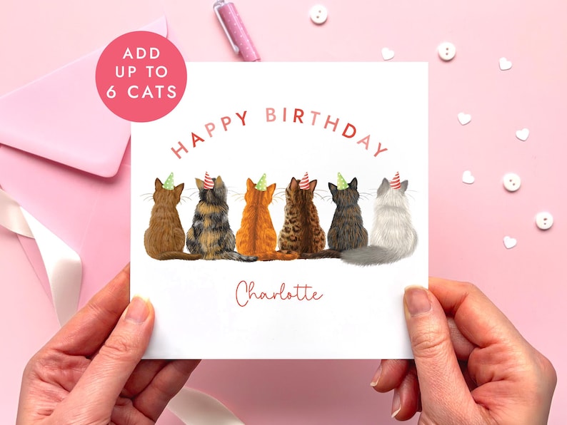 May include: A birthday card featuring six cats wearing party hats. The words "Happy Birthday" are arched across the top, with the name "Charlotte" below. A pink circle in the upper left corner reads "Add up to 6 Cats".