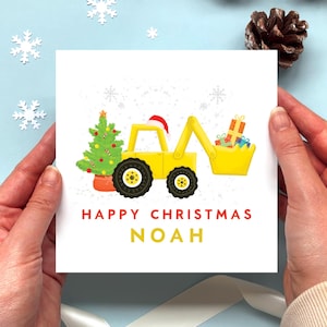 Könnte beinhalten: Eine quadratische Grußkarte mit einem gelben Bagger, der eine Weihnachtsmütze trägt und Geschenke in der Schaufel transportiert, neben einem geschmückten Weihnachtsbaum. Der Text lautet HAPPY CHRISTMAS NOAH in roten und gelben Buchstaben.