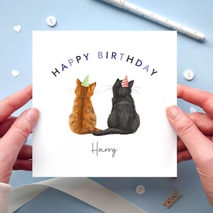 May include: A square birthday card featuring two cats wearing party hats. The text "HAPPY BIRTHDAY" is arched above the cats, with the name "Harry" written below. The cats are a ginger tabby and a black cat.