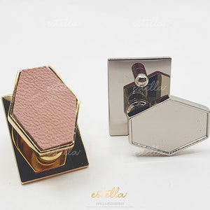 May include: Two hexagonal-shaped metal hardware pieces with a decorative knob. One piece is gold with a pink leather insert, the other is silver.