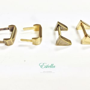 May include: Four gold-toned metal hardware pieces for leather crafting. Two are rectangular with two prongs on each side. Two are triangular with a bar in the middle.