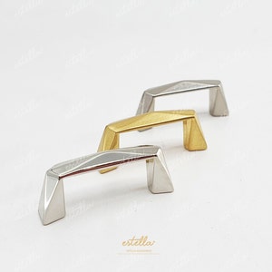 Könnte beinhalten: Drei geometrische Schrankgriffe in Silber-, Gold- und Messing-Finish. Die Griffe sind aus Metall und haben ein modernes, minimalistisches Design.