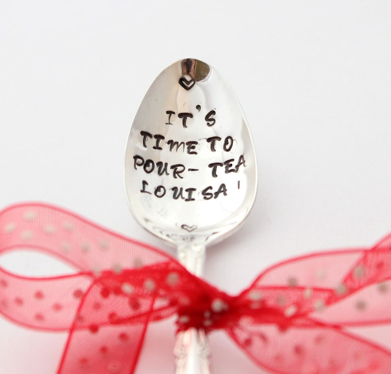 May include: A silver teaspoon with the words "It's time to pour tea Louisa" engraved on it. The spoon is tied with a red ribbon with white polka dots.