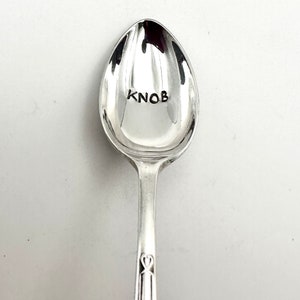 May include: A silver spoon with the word "Knob" engraved on the bowl. The spoon has a decorative heart design on the handle.