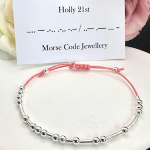 May include: A silver bracelet with a red string and silver beads. The bracelet is on a white surface. The text on the card reads "Holly 21st" and "Morse Code Jewellery".