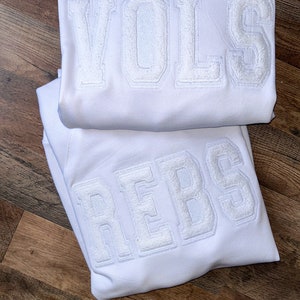 Peut inclure: Deux sweat-shirts blancs avec les mots "VOLS" et "REBS" en lettres blanches en relief.