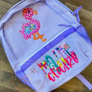May include: Purple and white striped backpack with a pink flamingo applique and the name "Claire" embroidered in colorful letters.