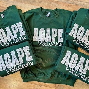 May include: Five green sweatshirts with white lettering that reads "Agape Pelicans" in a rhinestone design.