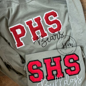 May include: Two long-sleeved shirts with embroidered school logos. The top shirt is green with a red and white "PHS Bears" logo. The bottom shirt is green with a red and black "SHS Bulldogs" logo.
