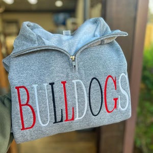 May include: A gray sweatshirt with a half-zip closure and the word "BULLDOGS" embroidered in red, white, and black.