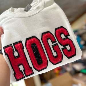 May include: White sweatshirt with a red and black embroidered patch that says "HOGS".
