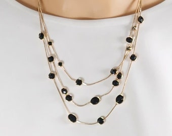 May include: A gold multi-strand necklace with black oval-shaped beads.