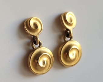 May include: A pair of gold-tone dangle earrings with a swirl design. The earrings are made of metal and have a polished finish.