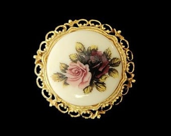 May include: A gold-toned brooch with a white porcelain cameo featuring a pink and purple rose floral design.