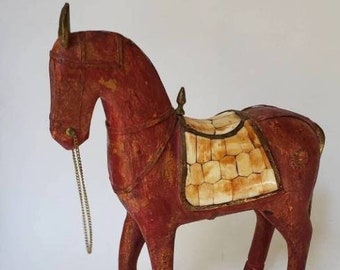 May include: A wooden horse figurine with a red painted body and a white bone saddle. The horse has a gold-colored bridle and reins.
