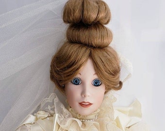 May include: A porcelain doll dressed in a white wedding gown with lace detailing. The doll has brown hair styled in a bun and blue eyes. She is holding a bouquet of white roses.