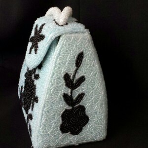 May include: A light blue beaded handbag with black floral embroidery. The bag has a triangular shape and a top handle.