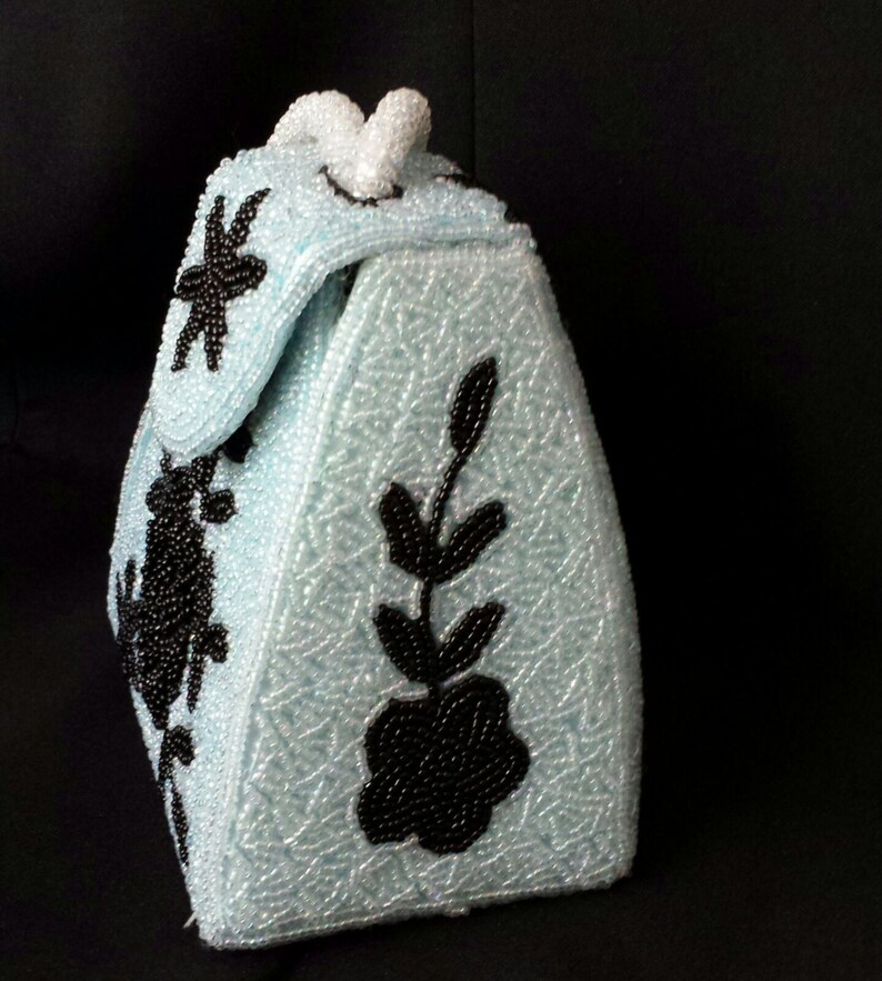 May include: A light blue beaded handbag with black floral embroidery. The bag has a triangular shape and a top handle.