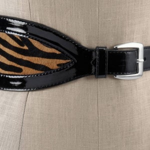 May include: A wide black patent leather belt with a zebra print insert. The belt has a silver buckle.