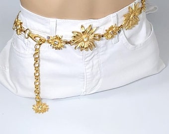 May include: A gold-tone chain belt with a dangling flower charm. The belt is adorned with multiple flower-shaped links, each featuring a sparkling rhinestone center.