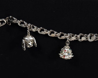 May include: A silver charm bracelet with a poodle charm and a Christmas tree charm with red, green, and blue rhinestones.