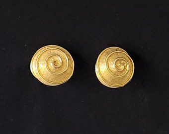 May include: A pair of gold-tone earrings with a spiral design. The earrings are round and have a textured surface.