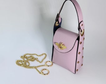 May include: A small pink leather handbag with a gold bee charm and a gold chain strap. The bag has a flap closure and is decorated with gold studs.