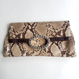 May include: A brown and beige snakeskin clutch with a silver oval-shaped clasp.