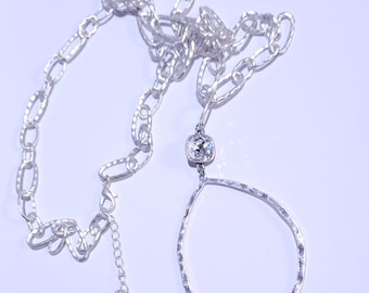 May include: A silver chain necklace with a large, clear crystal pendant. The pendant is shaped like a teardrop and has a textured surface. The chain is made of small, linked circles.