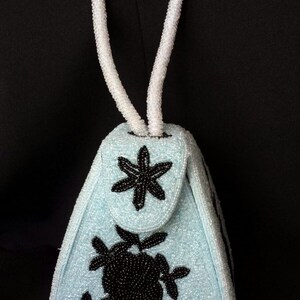 May include: A light blue beaded handbag with a white beaded handle and black floral embroidery.