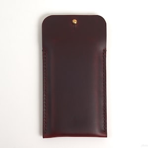 May include: A burgundy leather phone case with a brass button closure.