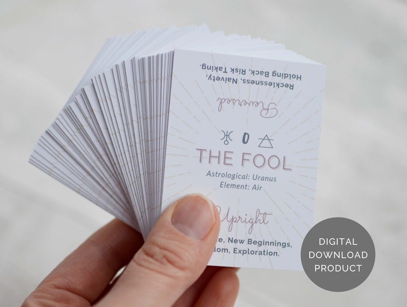 May include: A deck of tarot cards with a white background and pink text. The card shown is The Fool, with the astrological sign of Uranus and the element of Air. The card also includes the words "Upright" and "Reversed".