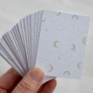 May include: A stack of white cards with a pattern of clouds, stars, and crescent moons in a light gray color.