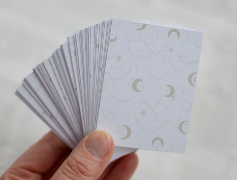 May include: A stack of white cards with a pattern of clouds, stars, and crescent moons in a light gray color.